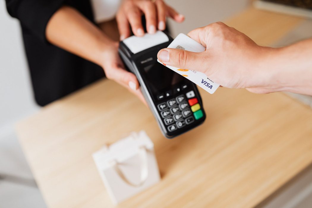 A hand holding a bank card against a payment terminal at a shop counter